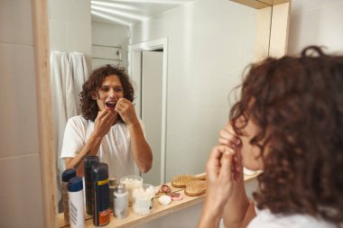 Banyoda dişlerini diş ipiyle fırçalayan bir adam.