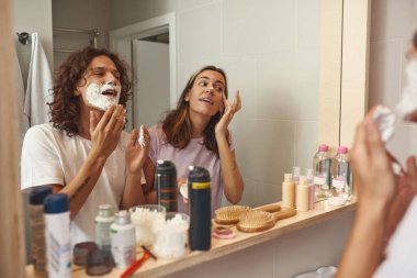 Adam tıraş köpüğü sürüyor ve kız kremi sürüyor.