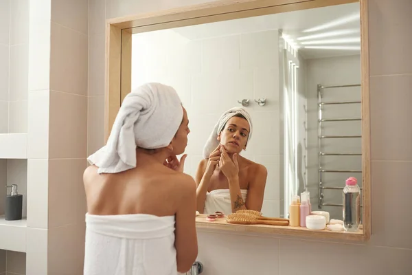 Mujer mirando su cara en el espejo en el baño — Foto de Stock