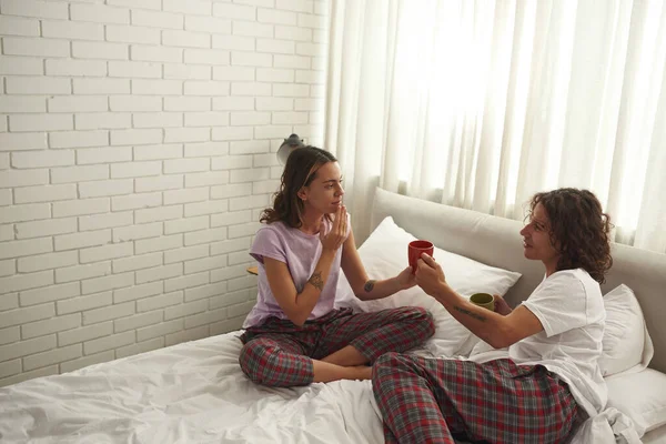 Guy giving cup with tea or coffee to girl on bed — Foto Stock