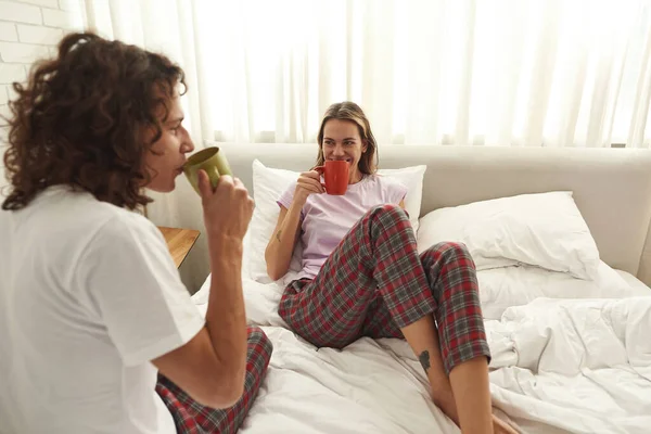 Cuplu tânăr bea ceai sau cafea și se odihnește pe pat — Fotografie, imagine de stoc