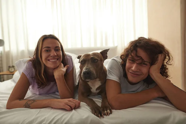 Pleased caucasian couple resting with dog on bed — Stock Photo, Image