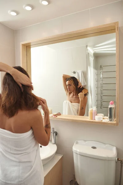 Young girl combing her hair with comb in bathroom — Foto de Stock