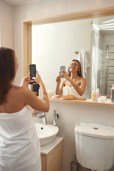 Woman taking photo of herself on phone in bathroom — Fotografia de Stock
