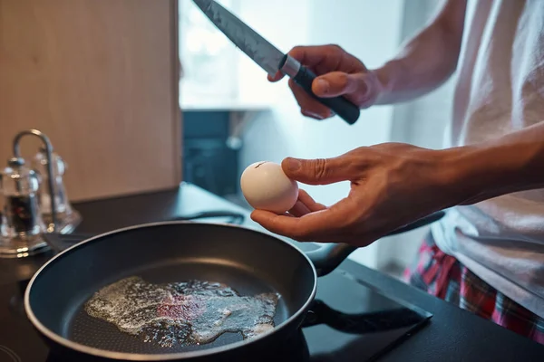 Man bryter ägg med kniv på pan under matlagning — Stockfoto