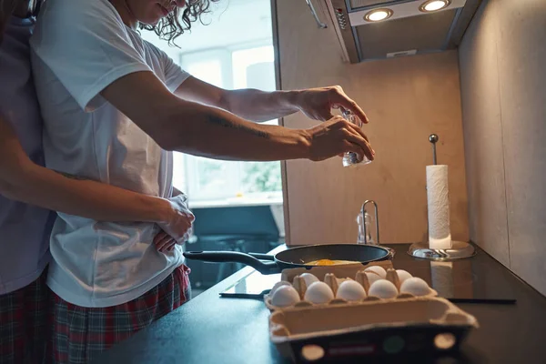 Girl hug guy throw salt on fried eggs on pan — Photo