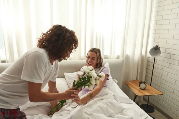 Man geven bloemen naar vriendin op bed in de ochtend — Stockfoto