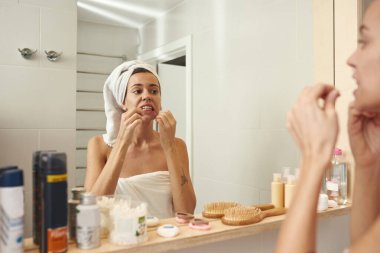 Banyoda dişlerini diş ipiyle fırçalayan bir kadın.