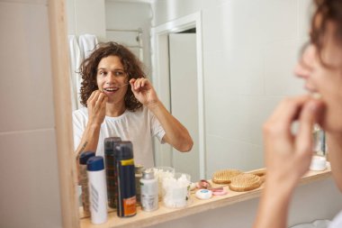 Dişlerini diş ipiyle fırçalayan genç bir adam.