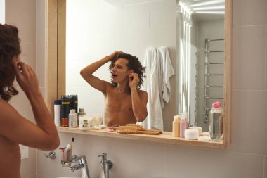 Genç adam banyoda kulak çubuğuyla kulak temizliyor.