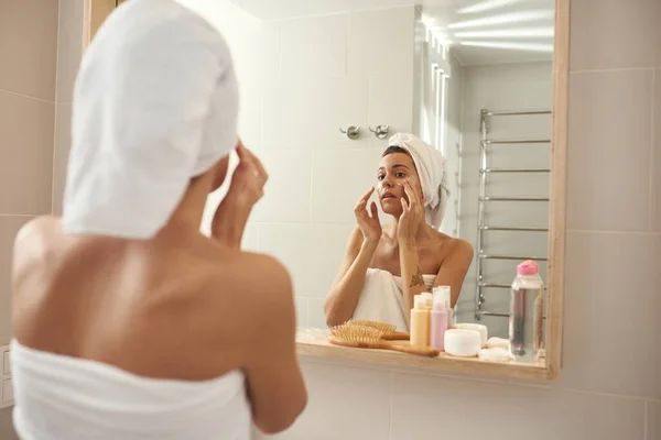 Mujer aplicar bajo parches en la cara del ojo en el baño — Foto de Stock