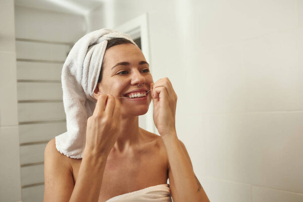 Mirror view of woman brush teeth with dental floss