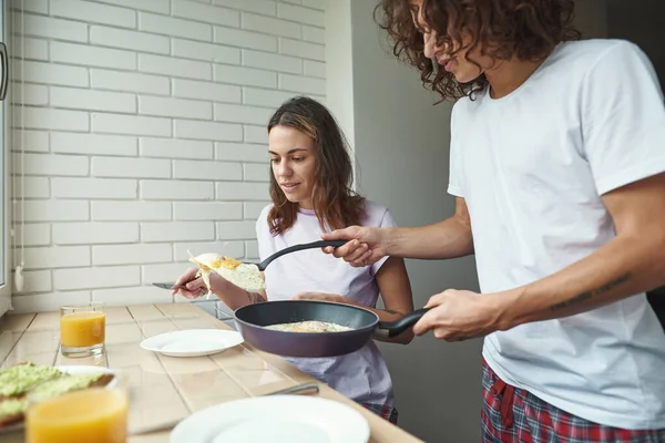 Man put fried eggs from pan on plate of girlfriend — Zdjęcie stockowe