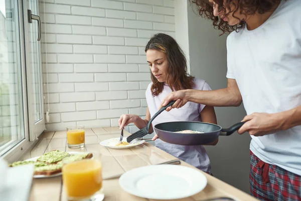 Man put fried eggs from pan on girl plate at home — Photo