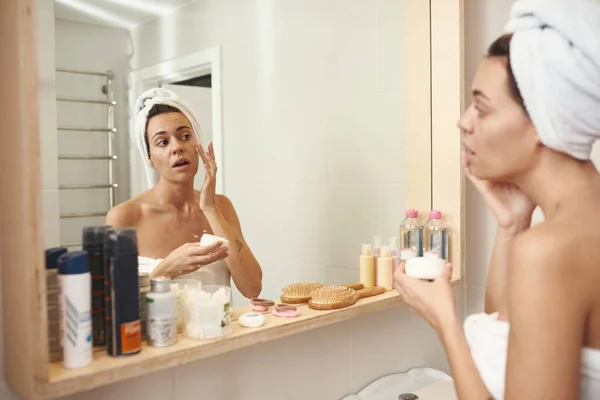Mujer untando crema cosmética en la cara en el baño — Foto de Stock