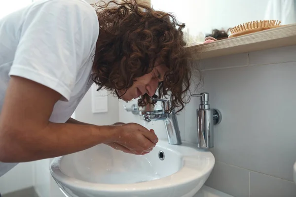 European man washing face with water in wash basin