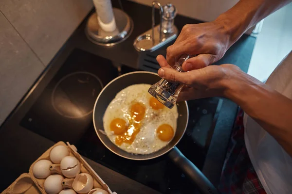 Man kastar peppar på stekta ägg på pan hemma — Stockfoto
