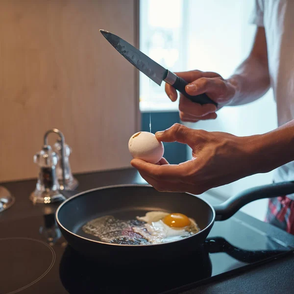 Частично человек разбивает яйцо с ножом на сковороде — стоковое фото