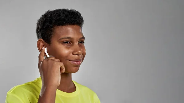 Nöjd svart pojke trycker trådlös hörlurar i örat — Stockfoto