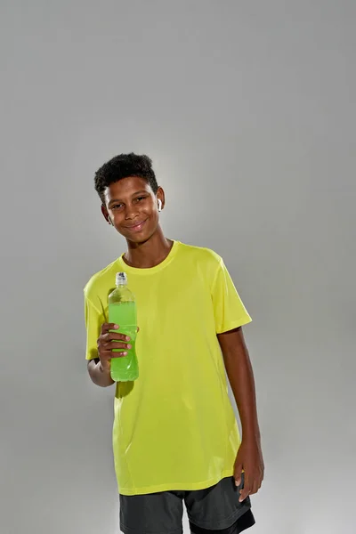 Sonriente chico negro con botella de bebida deportiva verde — Foto de Stock
