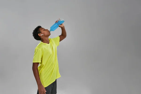 Vista lateral del chico negro bebiendo bebida deportiva azul — Foto de Stock