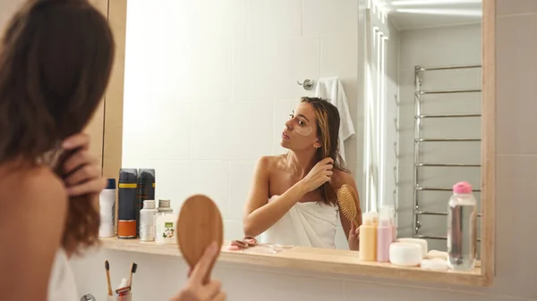 Mujer joven peinándose el pelo con peine en el baño — Foto de Stock