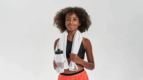 Mosolygós fekete lány törölközővel és vizes palackkal — Stock Fotó