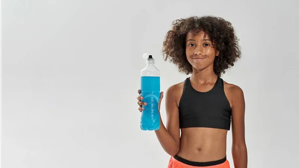 Sonriente chica negra con botella de bebida deportiva azul — Foto de Stock