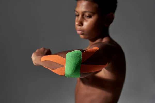 Black boy looking at injured elbow with plasters — Fotografia de Stock