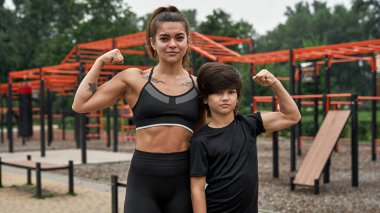 Kendine güvenen atletik anne ve oğlu kaslarını gösteriyorlar.