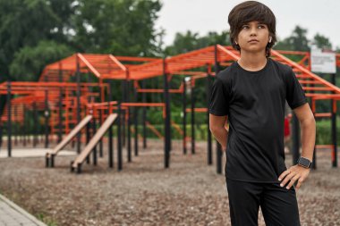 Odaklanmış sporcu çocuk, eli kalçasında, başka tarafa bakıyor.