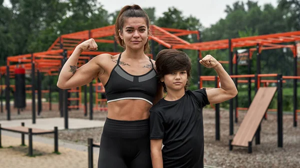 Kendine güvenen atletik anne ve oğlu kaslarını gösteriyorlar. — Stok fotoğraf