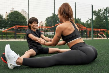 Anne ve oğlu spor sahasında birlikte esniyorlar.