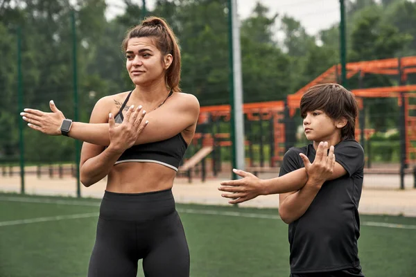 Anne ve oğlu spor sahasında birlikte esniyorlar.