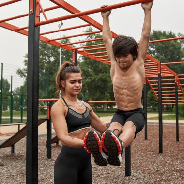 Anne oğluna yatay çubukta karın kası yapmayı öğretiyor.