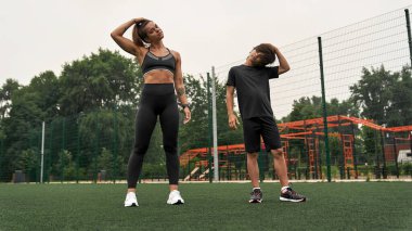 Anne ve oğlu spor sahasında boynunu uzatıyor.