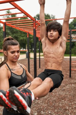 Beyaz tenli atletik anne oğlunun karın kaslarına yardım ediyor.