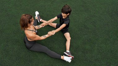Anne ve oğlu yeşil spor sahasında geriniyorlar.