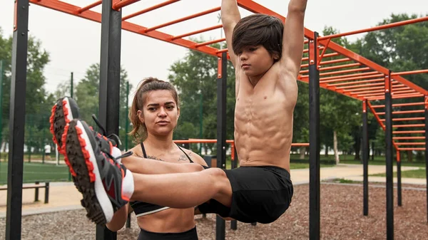 Kafkasyalı anne oğluna spor alanında karın kası yapmayı öğretiyor.