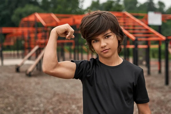 Seriös sport pojke visar biceps på idrottsplats — Stockfoto