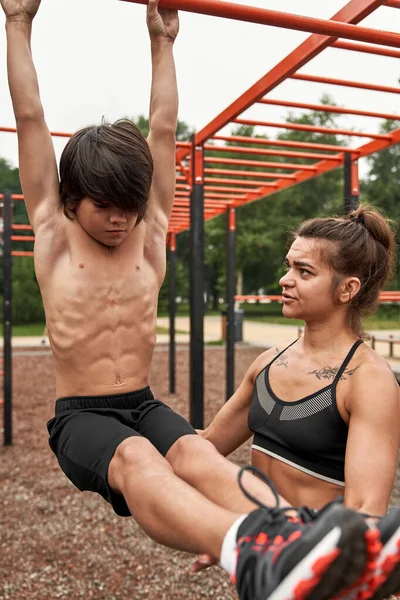 Anne oğluna yatay çubukta karın kası yapması için yardım et.