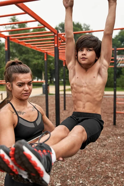 Beyaz tenli atletik anne oğlunun karın kaslarına yardım ediyor.
