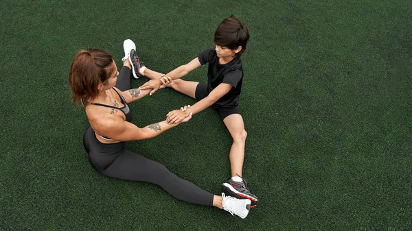 Anne ve oğlu yeşil spor sahasında geriniyorlar.