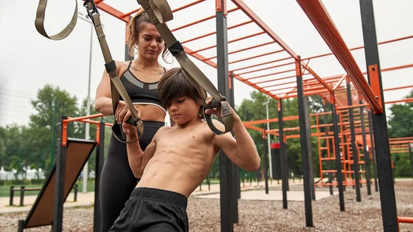 Mãe ajuda filho fazer exercício com tiras de suspensão — Fotografia de Stock