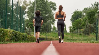 Anne ve oğlu yeşil parkta koşuyor.