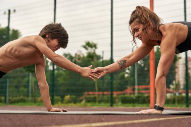 Anne ve oğul kalas egzersizi yapar ve el ele tutuşurlar.