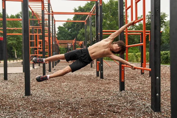 Boy do exercise on horizontal bar on sports ground — Fotografia de Stock