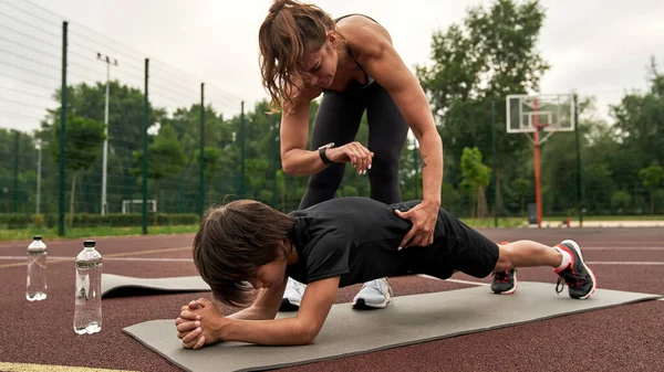 Atletik kadın, oğluna kalas yapmasında yardım ederken zamanı izliyor.