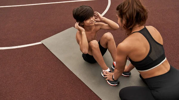 Kafkasyalı anne oğlunun spor paspası üzerinde çıtır çıtır çalışmasına yardım ediyor.