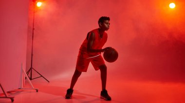 Kırmızı arka planda topu olan erkek basketbolcu